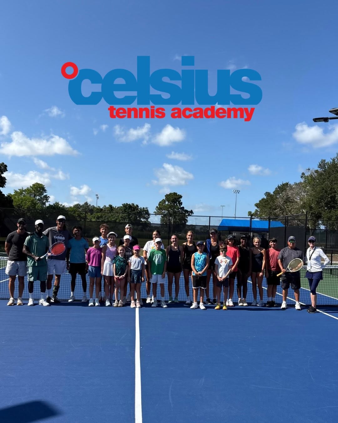 Group of kids and coaches posing for a photo on a blue tennis court, with a Celsius Tennis Academy logo in the sky above them.